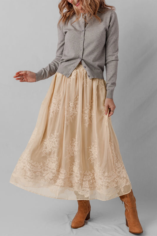 Woman wearing a gray shirt and beige lace skirt with brown boots on a plain background