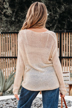 Woman wearing a beige knitted sweater and blue jeans standing outdoors.