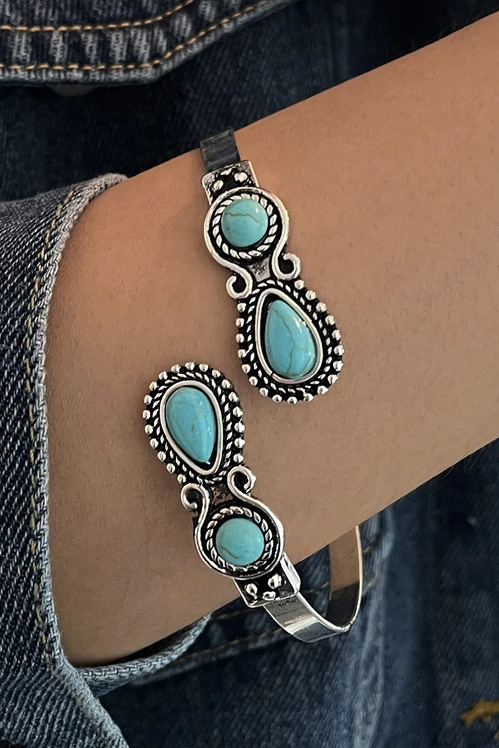 Silver bracelet with turquoise stones on a wrist against denim fabric.