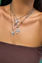 Close-up of a person wearing layered necklaces with cactus and bullhead designs.