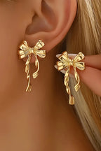 Gold bow-shaped earrings being worn on an ear with a blurred background