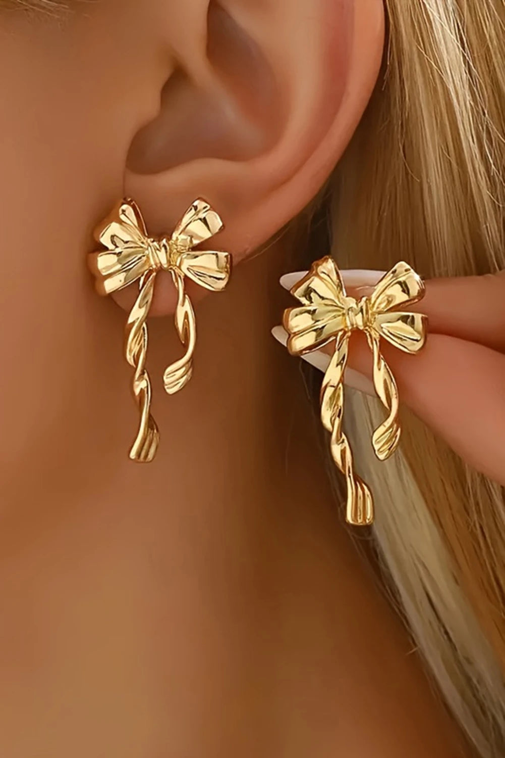 Gold bow-shaped earrings being worn on an ear with a blurred background