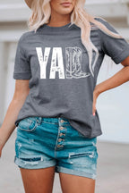 Person wearing a gray t-shirt with 'YA' and cowboy boot graphic, paired with denim shorts.