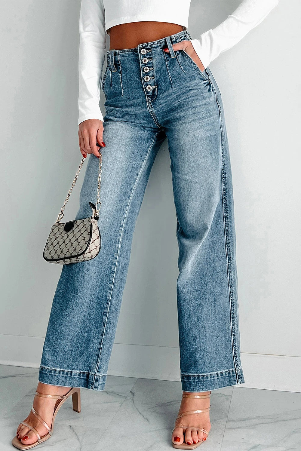 Person wearing blue jeans and a white top, holding a small handbag against a plain background