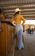 Woman in a yellow shirt and light blue jeans standing in a rustic indoor setting.